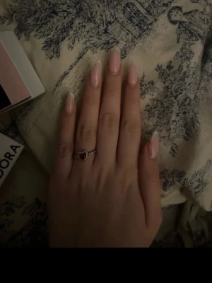 Pandora silverring med röd hjärtformad sten - Säljer en söt silverring från Pandora med en röd hjärtformad sten i mitten och små klara pärlor runt om hela ringen. Perfekt för dig som gillar romantiska detaljer och vill ha något unikt på fingret.osäker på storleken men löser innan jag skickar den