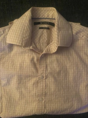 Beige rutig skjorta från Tiger - Säljer en beige rutig skjorta från Tiger med klassisk krage och knäppning framtill. Skjortan har diskreta rutor i vitt och beige och är i slim fit-modell. Perfekt för dig som gillar stilrena och tidlösa plagg.