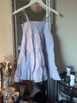 Ljusblå sommarklänning med volang - Söt ljusblå klänning med smala axelband och volangkant nedtill. Klänningen har en smockad överdel och är tillverkad i ett lätt, luftigt material som passar perfekt för varma dagar.