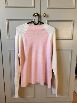 Ljusrosa stickad tröja Tommy Hilfiger - Snygg stickad tröja från Tommy Hilfiger i ljusrosa med vita ärmar och axelparti. Tröjan har rund halsringning och ribbstickade detaljer. Perfekt för dig som gillar en stilren och mjuk look. Stl (L) 