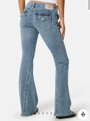 Helt nya JOEY LOW FLARE jeans från True Religion - Säljer ett par helt nya lågmidjade ljusblå bootcut jeans från True Religion, de har prislappen kvar och är i storlek w27 och är ungefär som storlek S, de är i färgen PEAK SPOT. Jeansen är tillverkade i mjuk denim med lätt stretch för skön passform och har ikoniska fickdetaljer bak. 