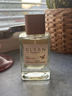 CLEAN Reserve Whipped Cherry parfym - En elegant parfym från CLEAN Reserve med doften Whipped Cherry. Flaskan är genomskinlig med en fyrkantig form och har en stilren träliknande kork. Etiketten är ljus med minimalistisk design och en liten fågelillustration. Innehåller eau de parfum. 100ml ny
