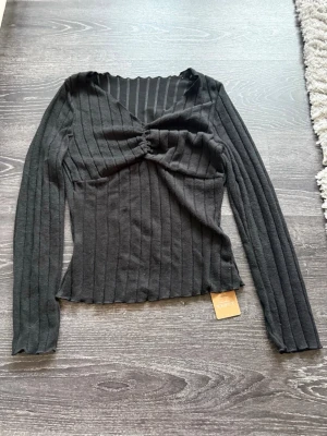 Svart ribbad topp med twist framtill - Trendig svart långärmad topp från shein med ribbad struktur och twistad detalj framtill. V-ringad hals och figurnära passform ger en snygg siluett. Perfekt för dig som gillar stilrena plagg med en twist.