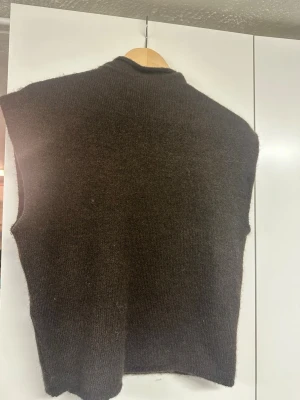 Mörkbrun stickad tröja Gina Tricot - Mysig mörkbrun stickad tröja från Gina Tricot i ullblandning. Tröjan har en enkel, rak passform och ribbad halsringning. Perfekt att bära över en skjorta eller t-shirt för en trendig lager-på-lager-look. Knappt använd (1-2 gånger)