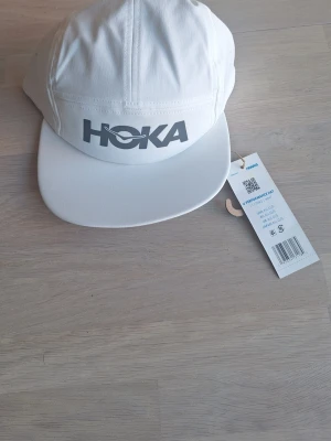Helt ny Vit keps från Hoka One size - Snygg, lätt och funktionell löparkeps som sitter som ett smäck. Den är enkel att justera med den smidiga dragskon.  Kepsen är gjord i ett luftigt tyg som leder bort fukten effektivt.