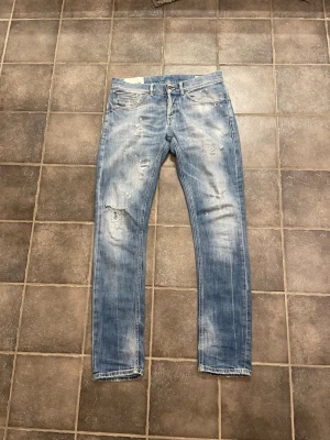 Dondup George  - Säljer ett par ljusblå jeans med slitningar och distressed detaljer. Jeansen har raka ben, klassisk femficksmodell och en tvättad look som ger en avslappnad vibe. Perfekta för dig som gillar en trendig och casual stil.