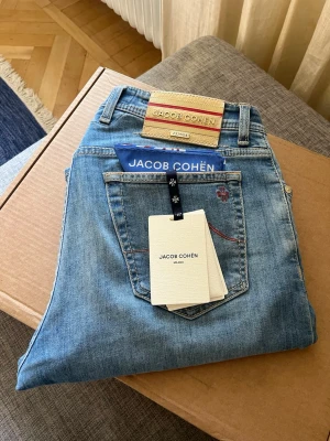 Jacob Cohën limited edition - Ljusblå jeans från Jacob Cohën i klassisk femficksmodell. Jeansen har en beige patch med röd logga bak, röd kontrastsöm på bakfickan och en liten broderad detalj. Tillverkade i mjukt denimtyg för en avslappnad look. Limited edition, nypris runt 10k, endast 554 par tillverkade