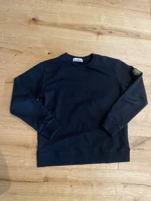 Svart långärmad tröja Stone Island - Säljer en svart långärmad tröja från Stone Island med klassisk patch på ärmen. Tröjan har rund halsringning och ribbade muddar vid ärmslut och nederkant. Perfekt för dig som gillar stilrena och ikoniska plagg.