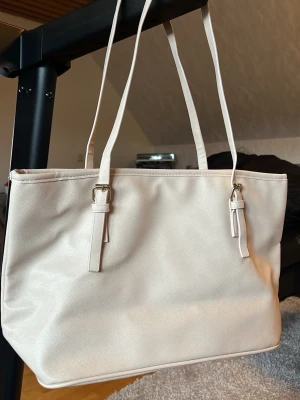 Beige-ljusrosa handväska - Stilren beige-ljusrosa handväska med långa axelband och guldfärgade detaljer. Väskan har en rymlig insida med innerfack och dragkedja samt magnetknäppning. Fått i present och aldrig kommit till användning