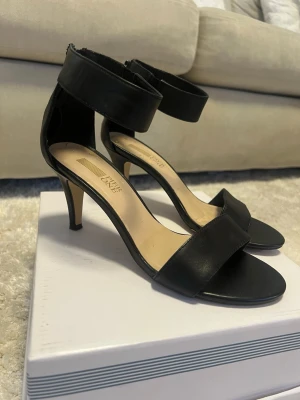 Svarta pumps från Pier one - Stilrena svarta pumps från Pier one med öppen tå, smal klack och breda remmar över foten och runt ankeln. Skorna har en elegant siluett och är tillverkade i ett slätt material som ger en klassisk look.