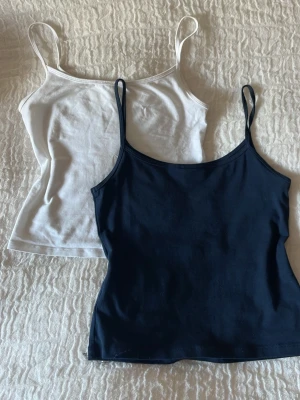 2-pack linnen från Gina Tricot - Säljer två klassiska linnen från Gina Tricot i storlek 134/140 men passar som Xs. Ett vitt och ett marinblått, båda med smala axelband och figurnära och croppad passform. Perfekta basplagg i mjuk bomull som funkar till allt.