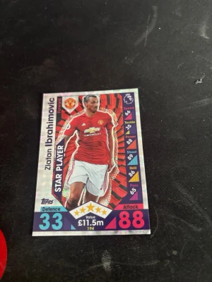 Match Attax Zlatan Ibrahimovic-kort - Samlar- och spelkort från Topps Match Attax med Zlatan Ibrahimovic i Manchester Uniteds röda matchtröja. Kortet har holografisk yta, visar spelarens stats och är märkt som Star Player. Perfekt för fotbollsfans och samlare.