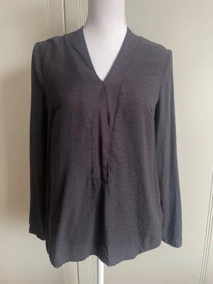 Brun blus från Saint Tropez - Snygg blus från Saint Tropez med v-ringning och långa ärmar. Blusen har en lös passform och är tillverkad i ett lätt, mjukt tyg som ger en skön känsla. Perfekt att styla med jeans eller kjol för en trendig look.