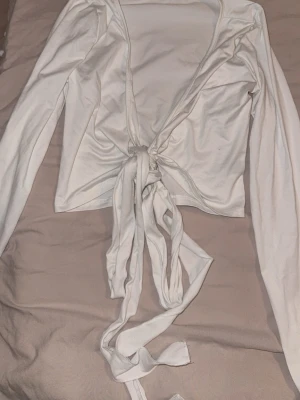 Vit omlottopp med knyt från SHEIN - Trendig vit omlottopp från SHEIN med långa ärmar och knyt framtill. Toppen är croppad och har en djup v-ringning som ger en snygg siluett. Perfekt att styla med höga jeans eller kjol för en cool look.