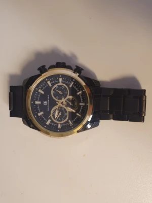 Svart och guld klocka från Daniel Klein - Medium storlek stilren klocka med svart länkarmband och urtavla. Klockan har guld detaljer runt boetten och på visarna. Urtavlan har flera små visare och tydliga markeringar. Perfekt accessoar för dig som gillar en klassisk men modern look.