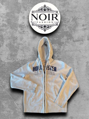 Zip hoodie från Hollister - Hollister hoodie med dragkedja. Stor tryckt logga i blått på bröstet med texten 'Hollister California'. Utrustad med huva och två fickor framtill. Perfekt för en avslappnad och cool stil.