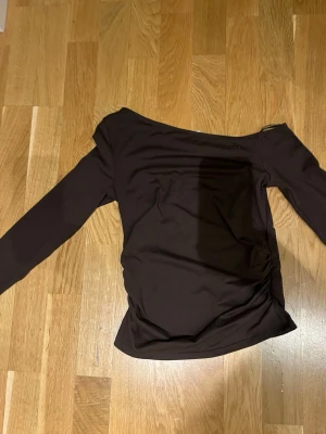 Brun off shoulder topp H&M Divided - Snygg brun långärmad off shoulder topp från H&M Divided. Tunn och stretchig i materialet, perfekt för att styla med jeans eller kjol. Enkel design med rynkade detaljer på sidan för en cool look.