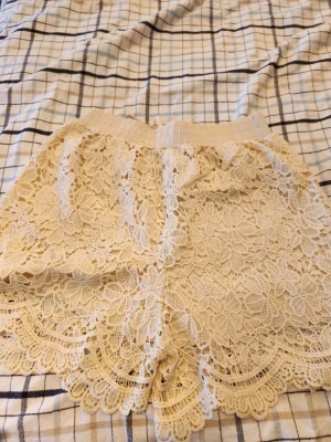 Beige virkade spets-shorts - Säljer ett par beige shorts med vacker virkad spets och elastisk midja. Shortsen har ett innerfoder och fina vågiga kanter längst ner. Perfekta för dig som vill ha en romantisk och bohemisk stil i sommar. Använda ca 1 gång men dem är inte min stil så dem får komma till någon annan nu!☺️