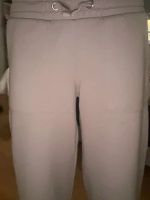 Beiga mjukisbyxor med dragsko - Säljer ett par beiga mjukisbyxor med resår i midjan och dragsko framtill. Byxorna har två bakfickor och är tillverkade i ett mjukt, bekvämt material. Perfekta för chill dagar hemma eller när du vill ha det extra comfy.