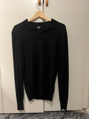 Svart långärmad tröja från Uniqlo - Klassisk svart långärmad tröja från Uniqlo med krage och knappslå framtill. Tröjan har ett skönt material, perfekt för dig som gillar en stilren look. 