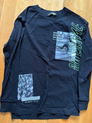 Svart långärmad topp från H&M - Cool svart långärmad topp från H&M med tryck i grått och grönt. Motiv med text och bilder på framsidan, bland annat 'Awesome' och 'Forever'. Rund halsringning och mjukt bomullsmaterial. Perfekt för dig som gillar streetstyle och grafiska prints.