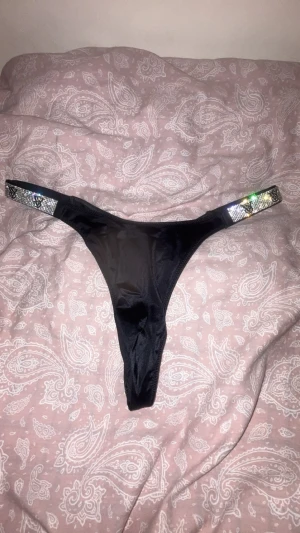 Victoria's Secret svarta stringtrosor - Ett par super snygga svarta stringtrosor som har låg midja. Glittriga band på sidan med deras logotyp ”VS”. Står M men passar även som S. Testat en gång med andra underkläder under.