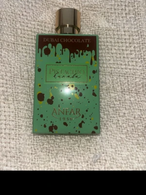 Pistachio Kanab Dubai Chocolate parfym - Unik parfym från Anfar med namnet Pistachio Kanab Dubai Chocolate. Flaskan är rektangulär i mintgrönt med bruna och gula färgstänk och har ett elegant guldfärgat lock. Designen ger en lyxig och modern känsla, perfekt för dig som gillar dofter med choklad och pistage.