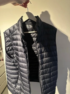 dunväst från boggi milano - Snygg svart dunväst från boggi milano med quiltad design och hög krage. Västen har dragkedja framtill och är lätt vadderad för extra värme. Perfekt att slänga över en hoodie eller tröja för en chill och stilren look.