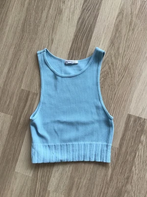 Ljusblå ribbad kort croppad topp i strechigt material, från Zara, stl XS - Ljusblå croppad linnetopp med ribbad struktur från Zara. Toppen är ärmlös och har en rund halsringning. Just nu fri frakt, så du betalar bara för toppen. Jag har fler plagg ute, och hittar du något mer från min garderobsutrensning, så skickar jag i samma paket.