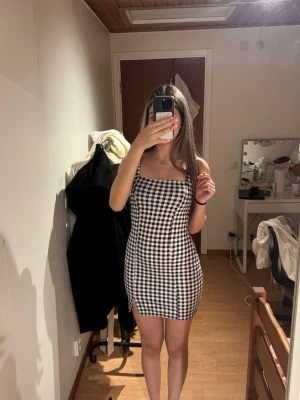 Svartvit rutig kort klänning - Säljer en svartvit rutig kort klänning med smala axelband och figurnära passform. Mycket gott skick, inga fläckar eller skador. 