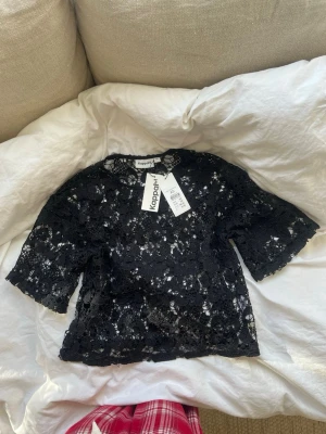 Svart spetsblus från Kappahl - Säljer en svart blus från Kappahl i genombruten spets med blommönster. Blusen har korta ärmar och rund halsringning. Perfekt för dig som vill ha en trendig och elegant topp med fina detaljer.
