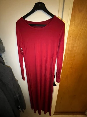 Röd långärmad långklänning - En enkel och stilren röd långklänning med långa ärmar och rund halsringning. Klänningen har en rak passform och är tillverkad i ett mjukt, stretchigt material som känns bekvämt mot huden. Perfekt för dig som gillar minimalistisk stil.