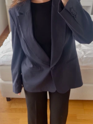 Mörkblå oversized kavaj - Marinblå kavaj med klassisk krage. Har 1 knapp framtill samt 2 fickor. Stilren modell med rak passform. Oanvänd med etikett kvar.