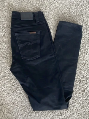 Nudie Jeans - Säljer ett par svarta slim fit jeans från Nudie Jeans med klassisk femficksmodell och diskret logga på bakfickan. Jeansen har raka ben och är tillverkade i ett stretchigt bomullsmaterial för skön passform. Skriv om du har frågor!