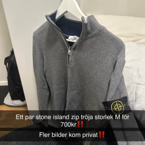 Grå ziptröja från Stone Island - Snygg grå ziptröja från Stone Island med ribbstickad struktur och hög krage i mörkblått. Tröjan har dragkedja framtill och den klassiska Stone Island-loggan på ärmen. Perfekt för dig som gillar streetwear och vill ha något stilrent.