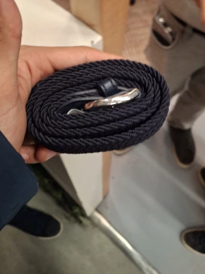 Mörkblått flätat bälte med silverdetalj - Snyggt mörkblått flätat bälte med en stilren silverfärgad metallspänne. Bältet är flexibelt och passar perfekt till jeans eller chinos. Enkel design som ger en clean look till outfiten.