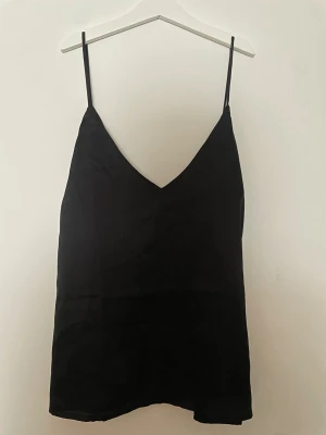 Svart linnetopp från 157 - Snygg svart linnetopp från 157 med tunna axelband och v-ringad hals. Perfekt att styla lager på lager eller bära som den är. Materialet känns mjukt och lätt, vilket gör toppen superbekväm och enkel att matcha.