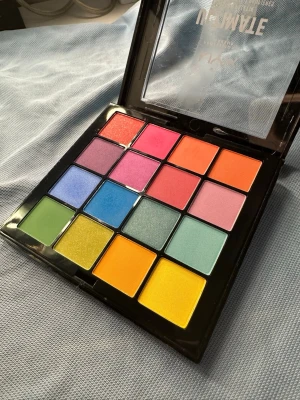 NYX Ultimate Brights ögonskuggspalett - Färgstark ögonskuggspalett från NYX med 16 intensiva nyanser i både matta och skimrande finish. Paletten innehåller allt från klara blå, gröna och gula toner till rosa, orange och lila. Perfekt för kreativa och lekfulla sminkningar. Kommer i en svart plastförpackning med genomskinligt lock. Aldrig använd, fick det i present. 