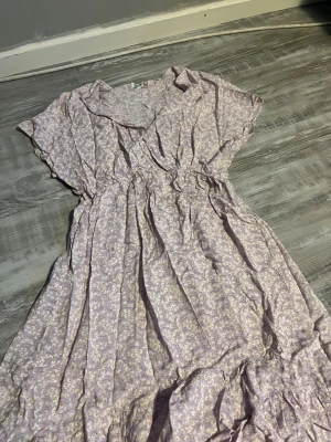 Klänning från missāy - Söt ljuslila klänning med blommigt mönster och volangdetaljer. Klänningen har korta ärmar, resår i midjan och är tillverkad i ett lätt bomullstyg. Perfekt för varma dagar och har en romantisk vibe.