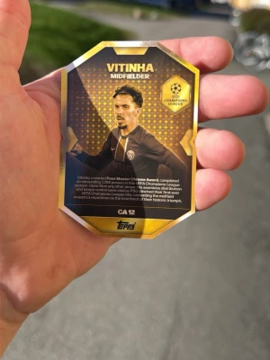 Pass Master fotbollskort Vitinha - Unikt fotbollskort från Topps med spelaren Vitinha, Pass Master Chrome Award Winner. Kortet har guld- och svart design med Champions League-logga och PSG-emblem. Text och bild på båda sidor, tillverkat i glansigt pappmaterial. Perfekt för samlare av sportkort. Ett exklusivt kort som inte finns många av.