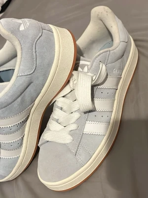 Adidas Campus ljusblå sneakers - Snygga Adidas Campus sneakers i ljusblå mocka med klassiska vita ränder och vit sula. Skorna har en låg profil, breda vita skosnören och gummisula i brunt. Perfekta för dig som gillar stilrena och tidlösa sneakers med retrovibbar. Priset är inte hugget i en sten så kom med bud. Storlek 42 typ använda 2-3 gånger så inget tecken på användning 