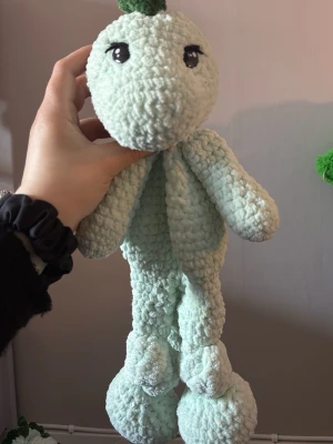 Virkad dinosaurie snuggler i mintgrönt garn - Söt handgjord dinosaurie i mjukt, mintgrönt garn med mörkgröna taggar längs ryggen och svansen. Stora safety ögon framtill och rundat huvud. Perfekt som eller gosedjur eller snutte. Unik och personlig presentidé till den lille 
