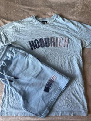 Ljusblått set från Hoodrich - Säljer ett ljusblått set från Hoodrich med t-shirt och shorts. Båda delarna har broderad HOODRICH-logga i vitt och mörkblått framtill. Setet är gjort i mjukt bomullsmaterial och har en avslappnad passform. Perfekt för en chill och trendig look.