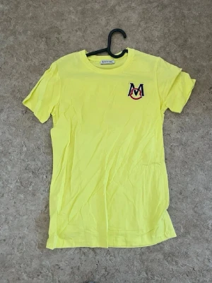 Gul t-shirt med broderad logga - Cool gul t-shirt från ENOSONE med broderad logga i blått och rött på bröstet. Klassisk rund hals och korta ärmar, perfekt för dig som vill sticka ut lite extra. Materialet är mjukt och känns skönt mot huden.