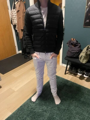 Svart cardigan från Moncler - Säljer en svart pufferjacka från Moncler med hög krage och dragkedja framtill. Jackan har quiltad design på framsidan och släta ärmar med ribbade muddar. Moncler-logga på vänster ärm. Perfekt för kalla dagar och riktigt snygg till streetwear. Den är köpt från mershsweden, har kvitto kvar, liten defekt vid vänster arm