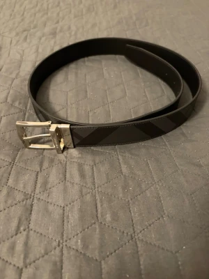 Svart och grått burberry skärp - Snyggt svart och grått bälte med rutigt mönster och silverfärgat spänne. Perfekt accessoar för att lyfta din outfit med en stilren touch. Bältet har klassisk design och passar till både jeans och kostymbyxor.