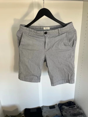 Randiga shorts från Selected Homme - Snygga grå shorts från Selected Homme med diskret randigt mönster. Klassisk passform med knapp och dragkedja framtill samt sidofickor. Hör gärna av dig vid frågor!