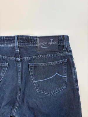 Mörkblå jeans från Jacob Cohen - Snygga mörkblå jeans från Jacob Cohen med klassisk femficksdesign och raka ben. Jeansen har en diskret logotyp på bakfickan och patch med varumärket i midjan. Perfekta för en stilren och avslappnad look.