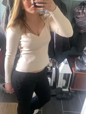 Beige långärmad topp med v-ringning - Snygg beige långärmad topp från H&M med v-ringad hals och figurnära passform. Tillverkad i mjukt material som känns skönt mot huden. Perfekt att styla med både jeans och kjol för en trendig look.