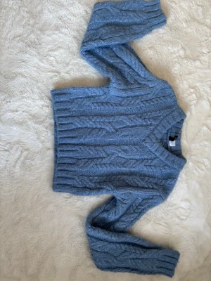 Blå kabelstickad tröja H&M Divided - Mysig blå kabelstickad tröja från H&M Divided. Tröjan har en croppad passform, rund halsringning och långa ärmar. Perfekt för lager-på-lager och enkel att styla till jeans eller kjol. Använt några gånger, pris kan diskuteras. 